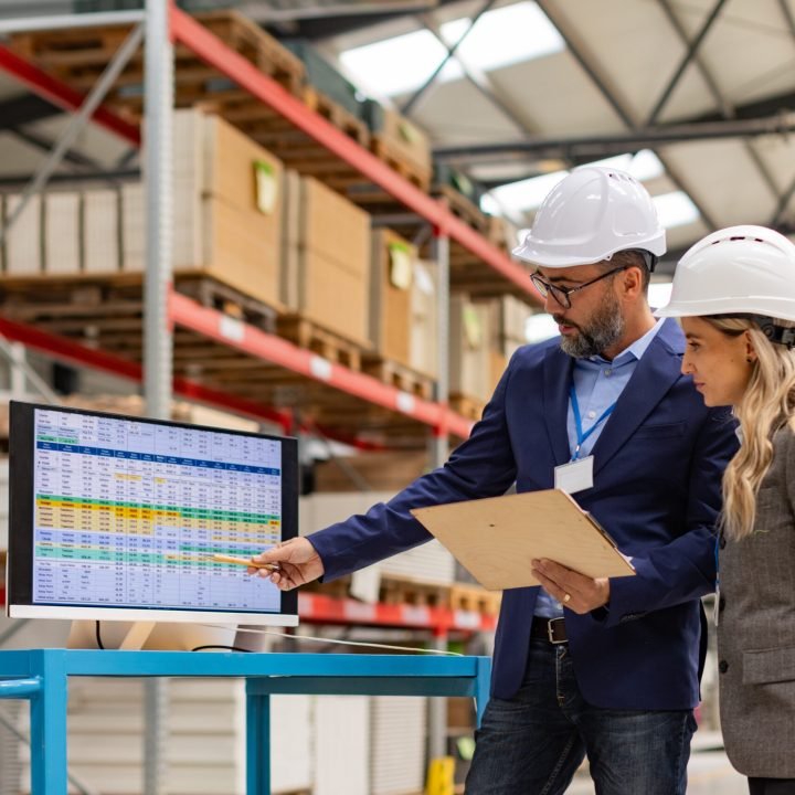 Rear view of female engineer and male project manager standing in modern industrial factory, talking about production. Team management in manufacturing facility