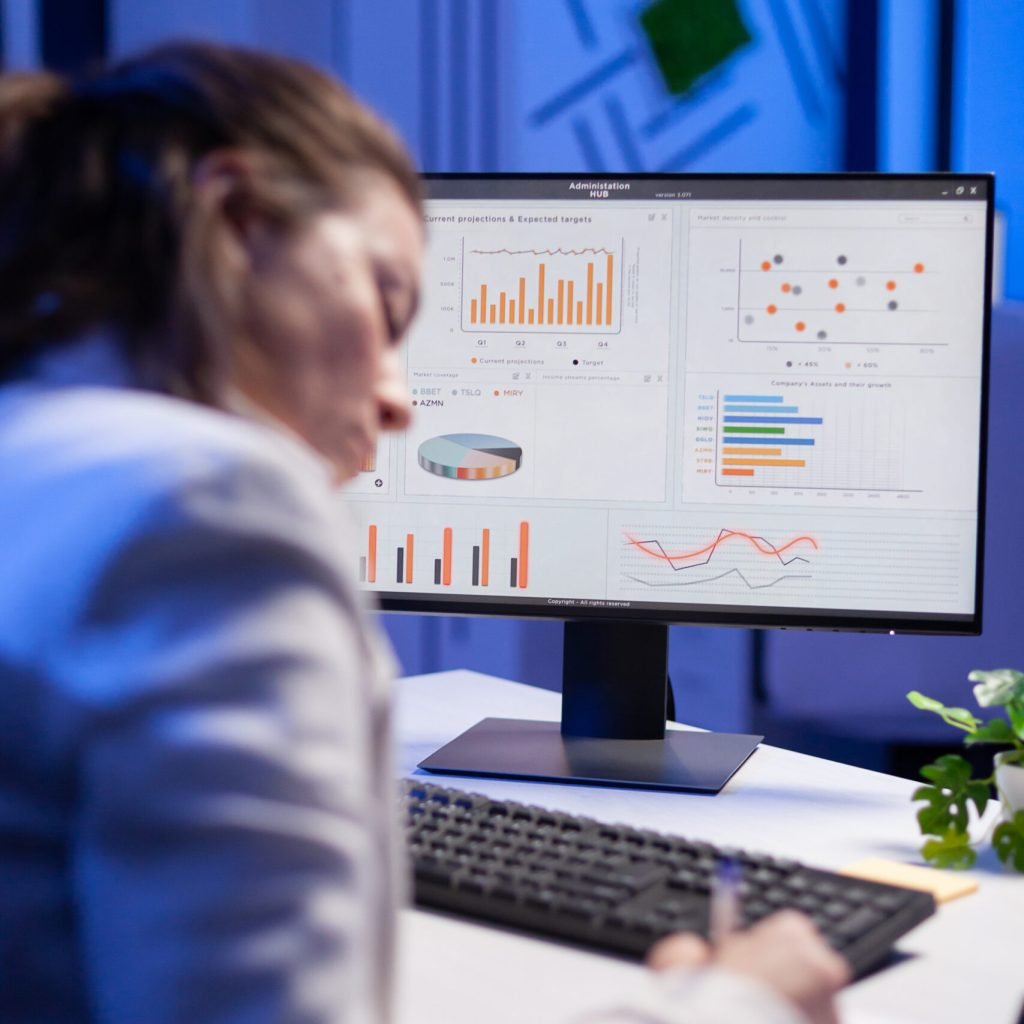 Tired entrepreneur trying to finish business project during internet videocall in front of computer, taking notes on notebook. Woman employee sitting at desk in workplace working at marketing ideas